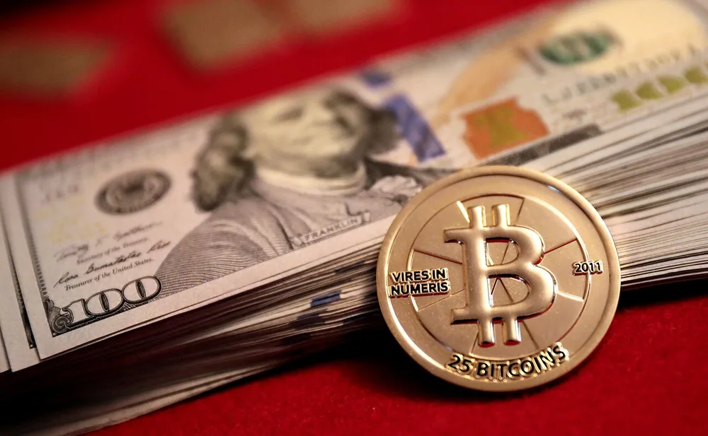 A 25-bitcoin gold Casascius coin resting on US $100 bills.