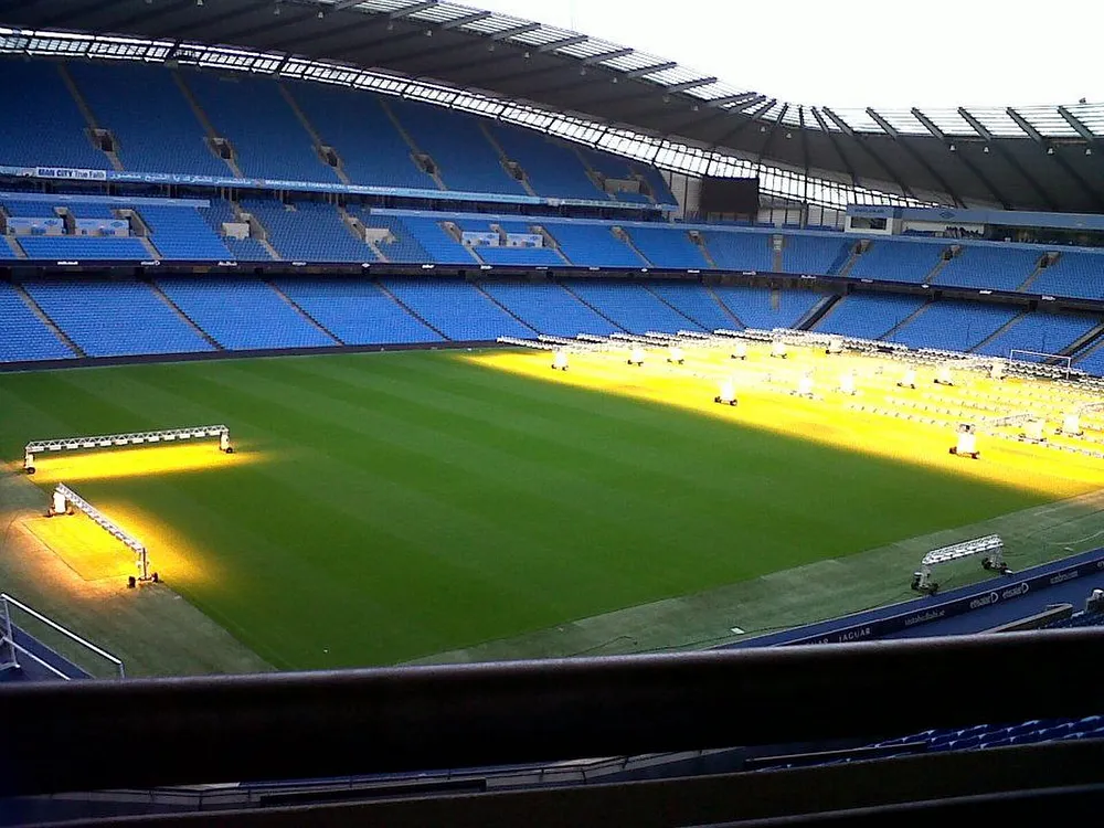 Empty sky-blue seats and turf grow lights on the pitch at Etihad Stadium in Manchester. Photo: Bradley Michael / geograph.org.uk, CC BY-SA 2.0.