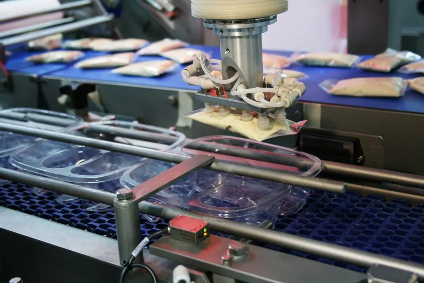 A robotic arm lifts sealed food pouches on an automated packaging assembly line. Photo: Yingz / Wikimedia Commons, CC BY-SA 4.0.
